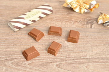 A chocolate candy bar broken into pieces with the wrappers out of focus