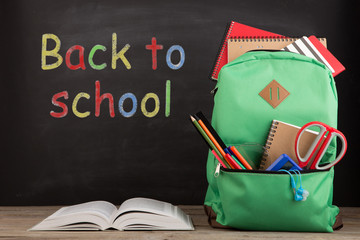 Education concept - school backpack with books and other supplies, blackboard background