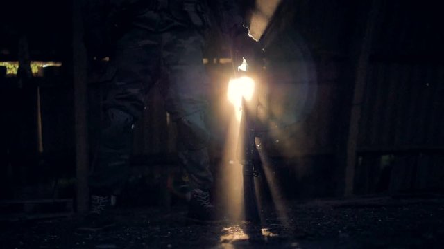 A man in army fatigues stands and leans on his rifle. 