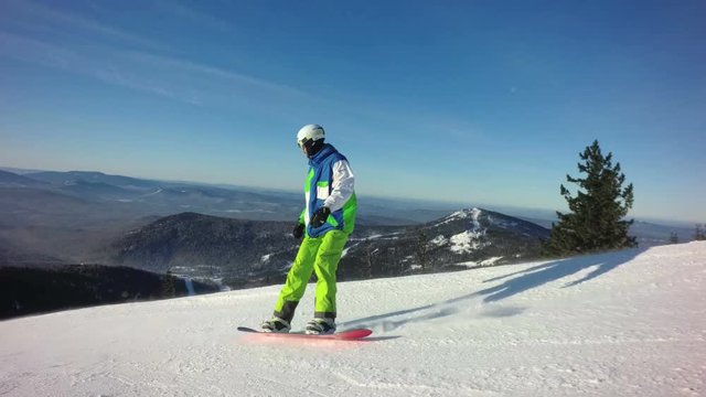 Snowboarder rides down the peak of a mountain in sunny winter day
