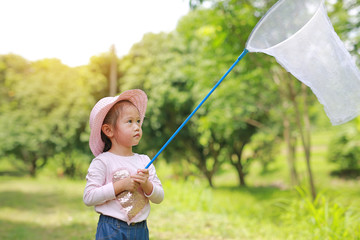 Adorable little asian girl wear straw hat in a field with insect net in summer.