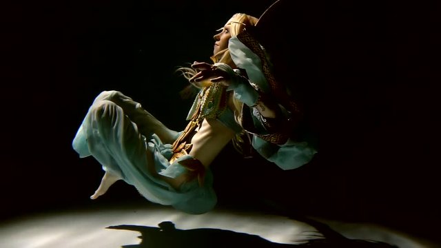 Slow motion. Slender blonde girl in the armor and dress of the elf drifts under water looks at the rays of the sun