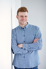 Fototapeta premium Cheerful handsome redhead young guy in black cardigan checkered shirt photographed against white wall in the studio