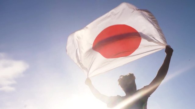 Young man holding japanese national flag to the sky with two hands at the beach at sunset japan