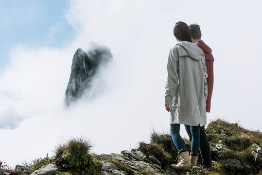 Couple in white and red raincoats overlooking a mountain top in the clouds in Switzerland