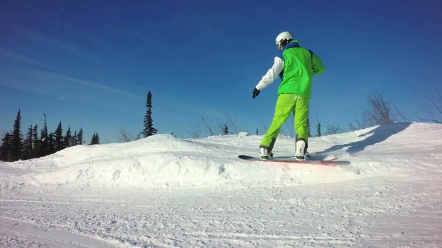 Man snowboarder is riding down the top of a mountain in sunny winter day