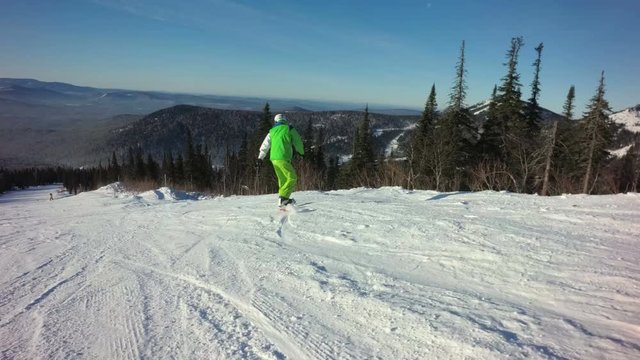 Man snowboarder is riding fastly down the top of a mountain in sunny winter day