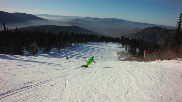 Man snowboarder rides fastly down the top of a mountain in sunny winter day