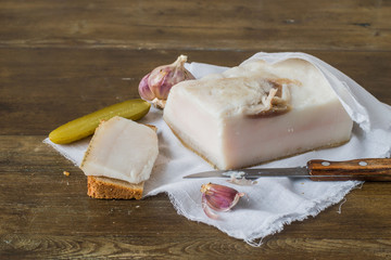 A piece of salted lard and black rye bread on a white cotton napkin on an old wooden table. 