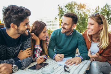 Group of four friends having fun a coffee together. Two women and two men at cafe talking laughing and enjoying their time