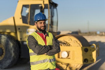 Bearded construction worker posing ner to steam roller machine