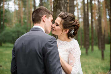 The first kiss of a newly formed family. Beautiful bride and handsome man groom kissing in a forest of pine trees.