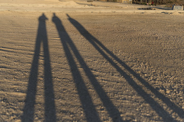 three shaodws of walking people in the sand at sunset