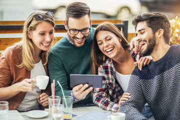 Group of four friends having fun a coffee together. Two women and two men at cafe talking laughing and enjoying their time