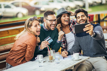 Group of four friends having fun a coffee together. Two women and two men at cafe talking laughing and enjoying their time