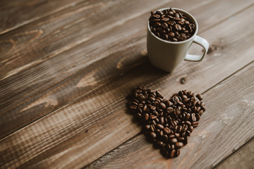 Roasted coffee beans in white cup at wood background and concept coffee love heart