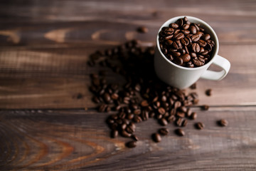 Roasted coffee beans in white cup at wood background