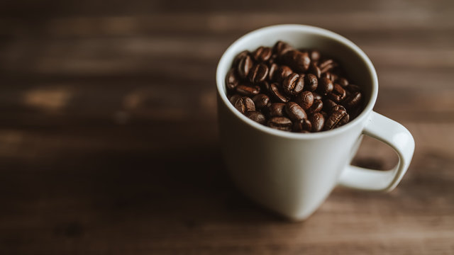 Roasted coffee beans in white cup at wood background