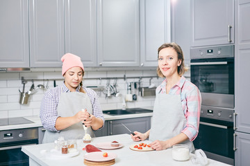 Two professionals cutting fresh strawberries and making whipped cream to decorate cakes