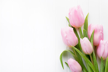 Fresh pink tulip flowers bouquet on shelf in front of wooden wall.