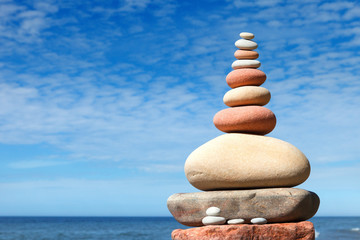 Fototapeta na wymiar Rock zen pyramid of white and pink stones on a background of blue sky and sea.