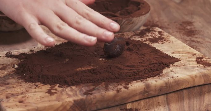 Slow motion handheld shot put truffles in cocoa powder on board