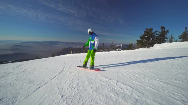 Man snowboarder in bright clothes rides down the top of a mountain at winter sunny day