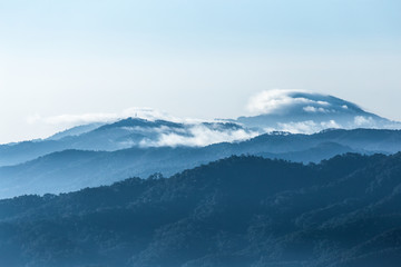 Peak and eadge of blue mountains covered by fog and clouds with bright sky in winter season.