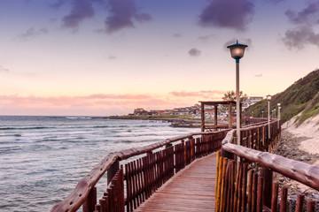Boardwalk führt bei Sonnenuntergang am Strand und Meer in Gonubie vorbei