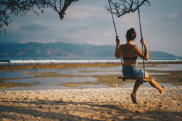 Frau sitzt auf einer Schaukel am Strand