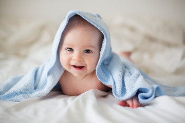 Cute little baby boy, relaxing in bed after bath, smiling happily - obrazy, fototapety, plakaty