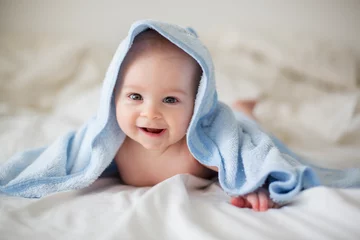 Fototapeten Cute little baby boy, relaxing in bed after bath, smiling happily © Tomsickova