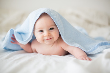 Cute little baby boy, relaxing in bed after bath, smiling happily - obrazy, fototapety, plakaty