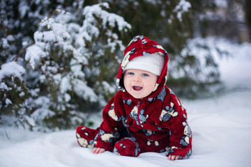 Little cute smiling baby boy, sitting outdoors in the snow