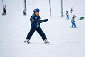 Fototapeta na wymiar Cute little preschool child in blue jacket, skiing happily on a sunny day