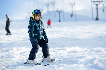 Fototapeta na wymiar Cute little preschool child in blue jacket, skiing happily on a sunny day
