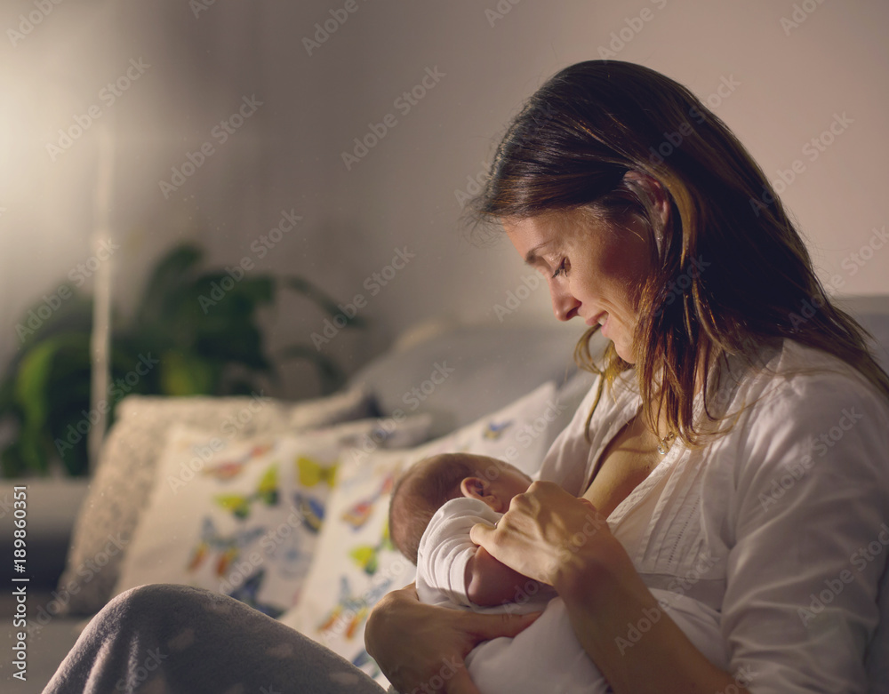 Wall mural Young beautiful mother, breastfeeding her newborn baby boy at night