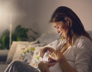 Young beautiful mother, breastfeeding her newborn baby boy at night
