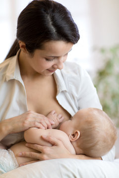 Young mother holding her newborn child. Mom nursing baby. Pretty woman breastfeeding kid.