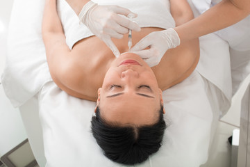 Obraz na płótnie Canvas Top view of relaxed mature woman taking botox injection. She is lying in chair at spa. Her eyes are closed