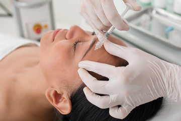 Close up of tranquil mature woman taking collagen injection in beauty salon. She is lying on the couch while taking procedure. Her eyes are closed