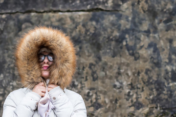 Portrait of a young woman in a fur jacket against a wall grunge background