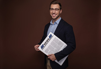 Portrait of beaming male keeping newspaper in arm. Information concept. Isolated