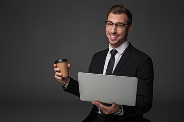 Portrait of outgoing unshaven male drinking cup of coffee while working with laptop. Rest and job concept. Isolated