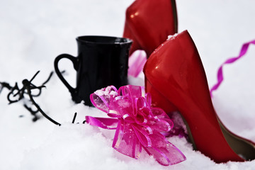 Red shoes with a cup and bow on white snow in a circle of barbed wire
