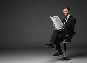 Full length portrait of outgoing bearded worker looking trough article while locating on seat....