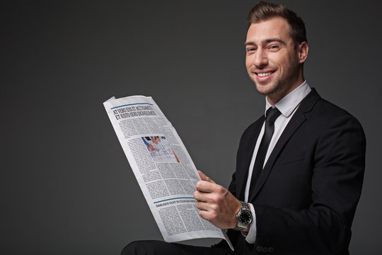 Portrait of cheerful unshaven businessman reading newspaper. He looking at camera. Rest and information concept. Isolated