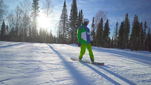 Sportsman snowboarder in bright clothes is riding down from the top of a hill at winter sunny day