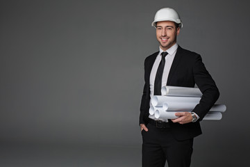 Portrait of cheerful bearded architect holding different rolls of paper with plans. Construction...