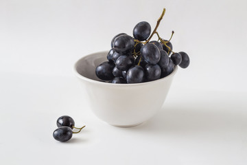 Black grapes in a white ceramic bowl on a light background